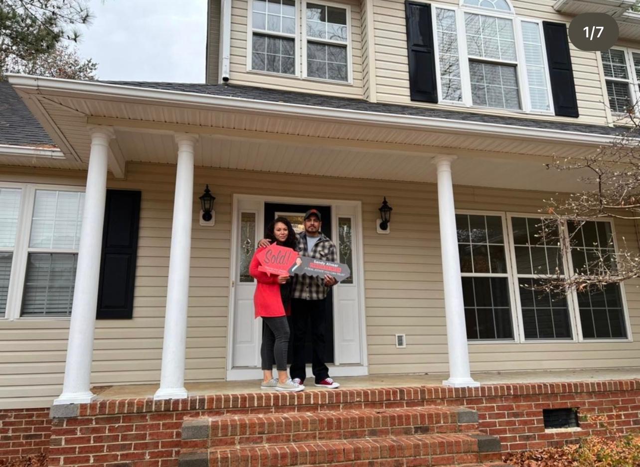 Couple with Sandy Alvear Sold sign at their new home